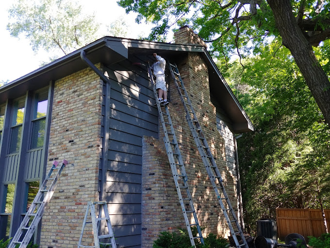 McCABE PAINTING contractor painting two-story building exterior on ladder.